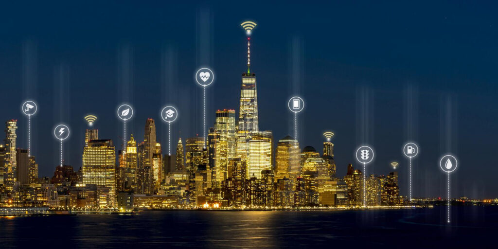 The image shows a beautiful night panorama of New York with the typical icons of a smart city (wifi, smart grids, intelligent traffic control, etc.)